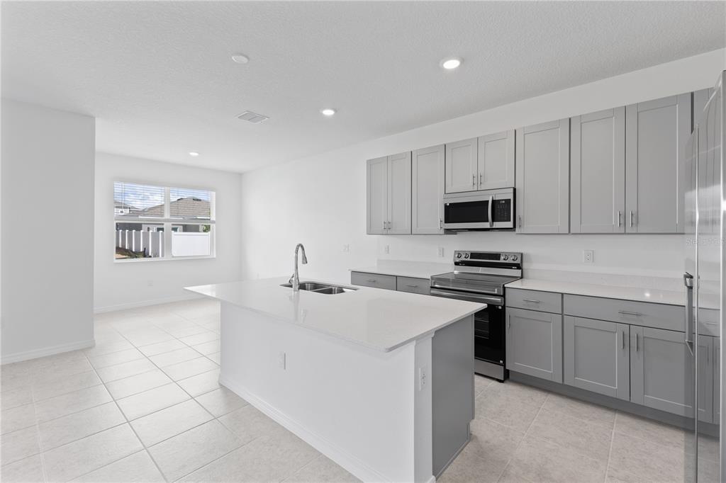 A modern kitchen features gray cabinets, white countertops, a central island, and tile flooring — 495 SILVER PALM DRIVE, HAINES CITY, FL