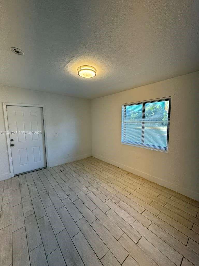 An empty room features white walls, a light-colored tiled floor, a window, and a door — RIVIERA BEACH, FL