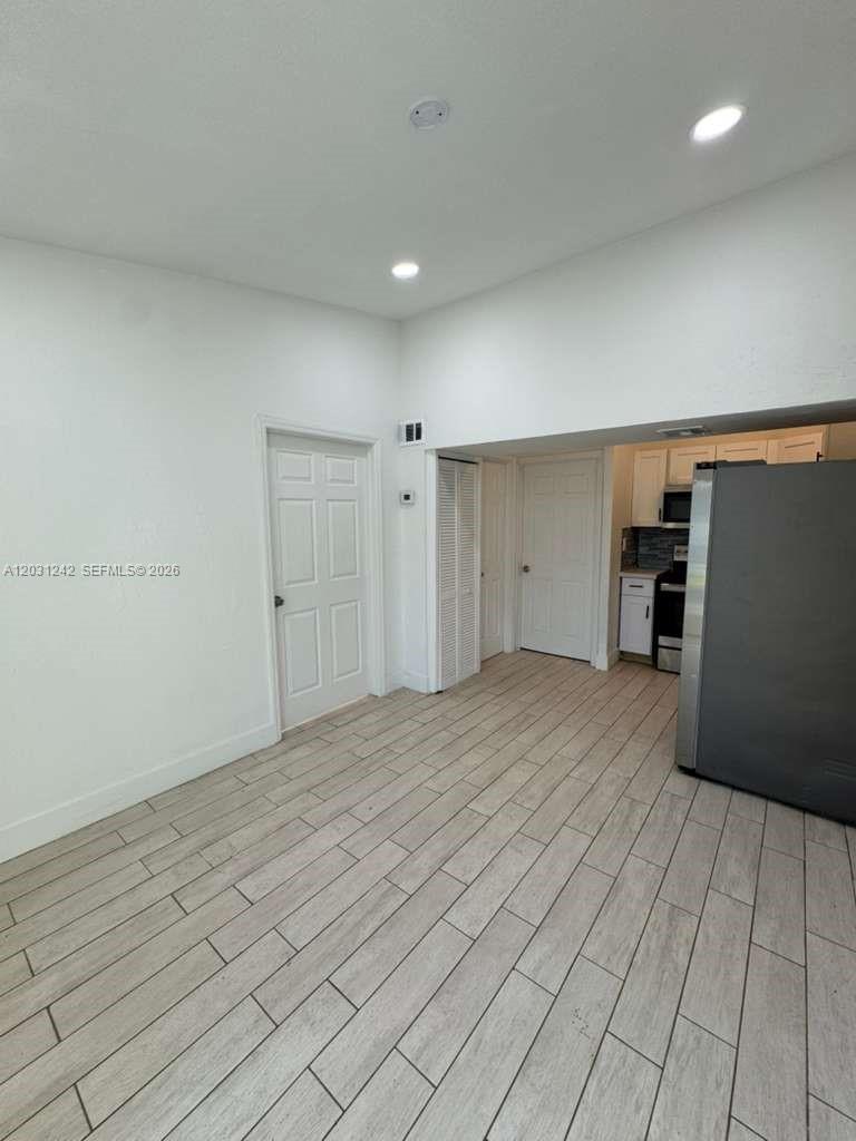 A room with light wood-look tile flooring leads to a kitchen with stainless steel appliances — RIVIERA BEACH, FL