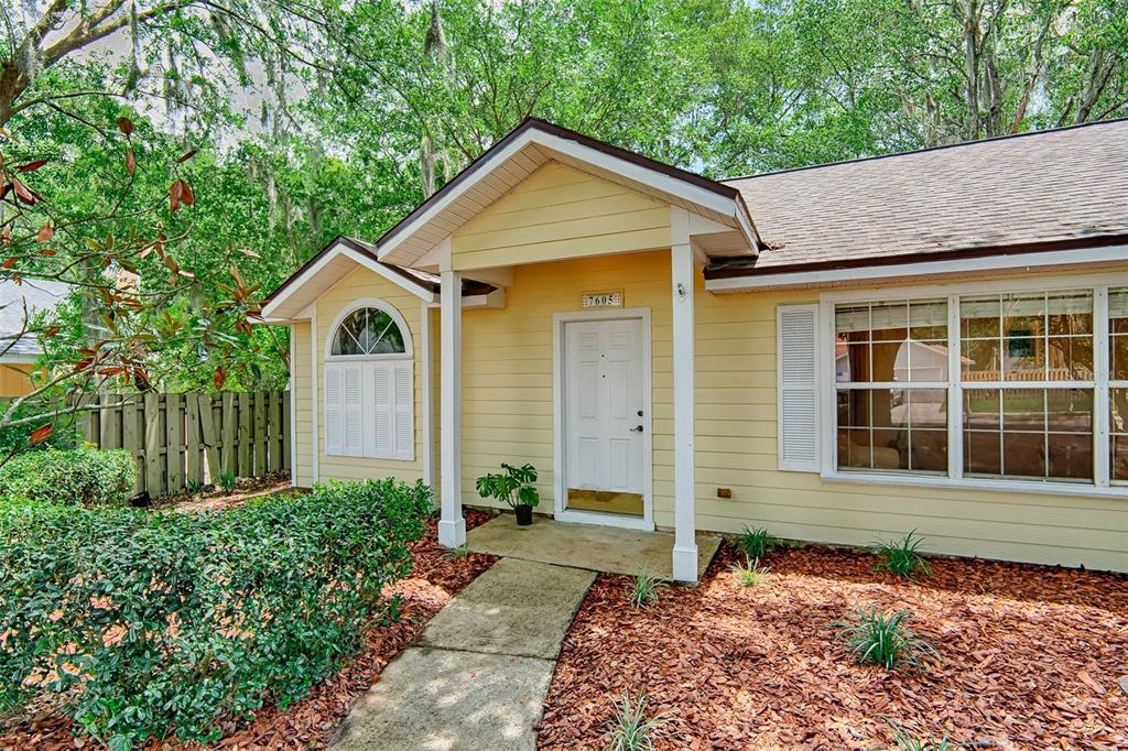 A yellow house exterior features a covered entryway, a white front door, and landscaping — 7605 SW 51ST BOULEVARD, GAINESVILLE, FL