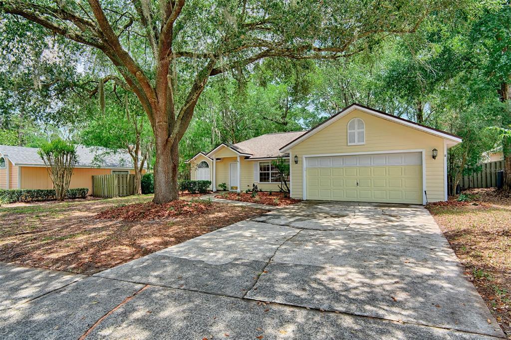 A yellow single-story house with a two-car garage and a large tree in the yard — 7605 SW 51ST BOULEVARD, GAINESVILLE, FL
