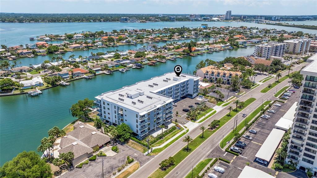 An aerial view shows a multi-story white apartment building situated along a waterfront canal — 415 ISLAND WAY UNIT 502, CLEARWATER BEACH, FL