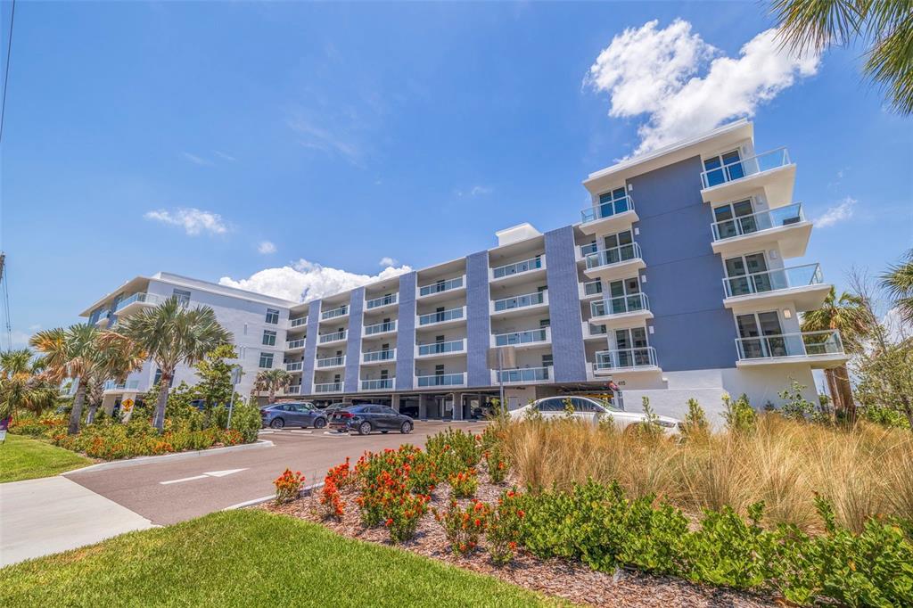 A multi-story apartment building with blue siding and balconies stands above a ground-level parking area — 415 ISLAND WAY UNIT 502, CLEARWATER BEACH, FL