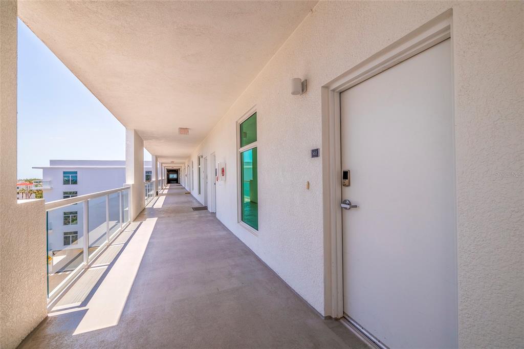 An outdoor apartment hallway with a white door, glass railing, and concrete flooring — 415 ISLAND WAY UNIT 502, CLEARWATER BEACH, FL