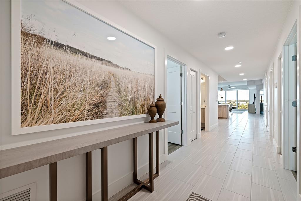 A bright hallway features a console table, large landscape art, and light-colored tile flooring — 415 ISLAND WAY UNIT 502, CLEARWATER BEACH, FL