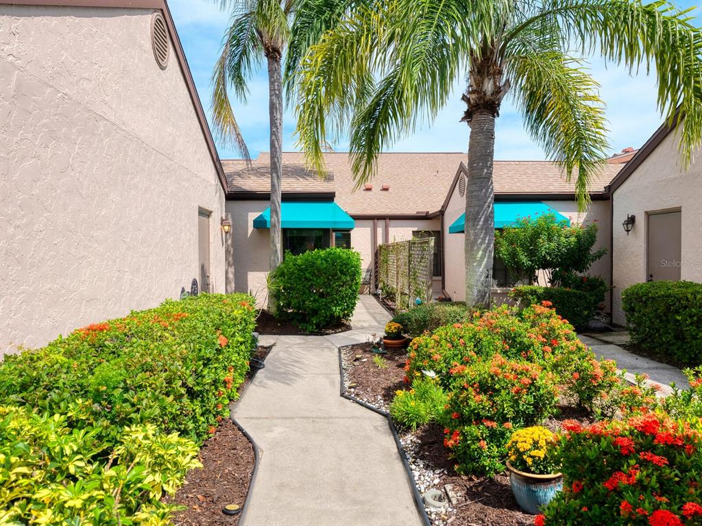 A concrete walkway leads between two tan buildings with palm trees and flowering bushes — 6103 CLUBSIDE DRIVE UNIT 6103, SARASOTA, FL