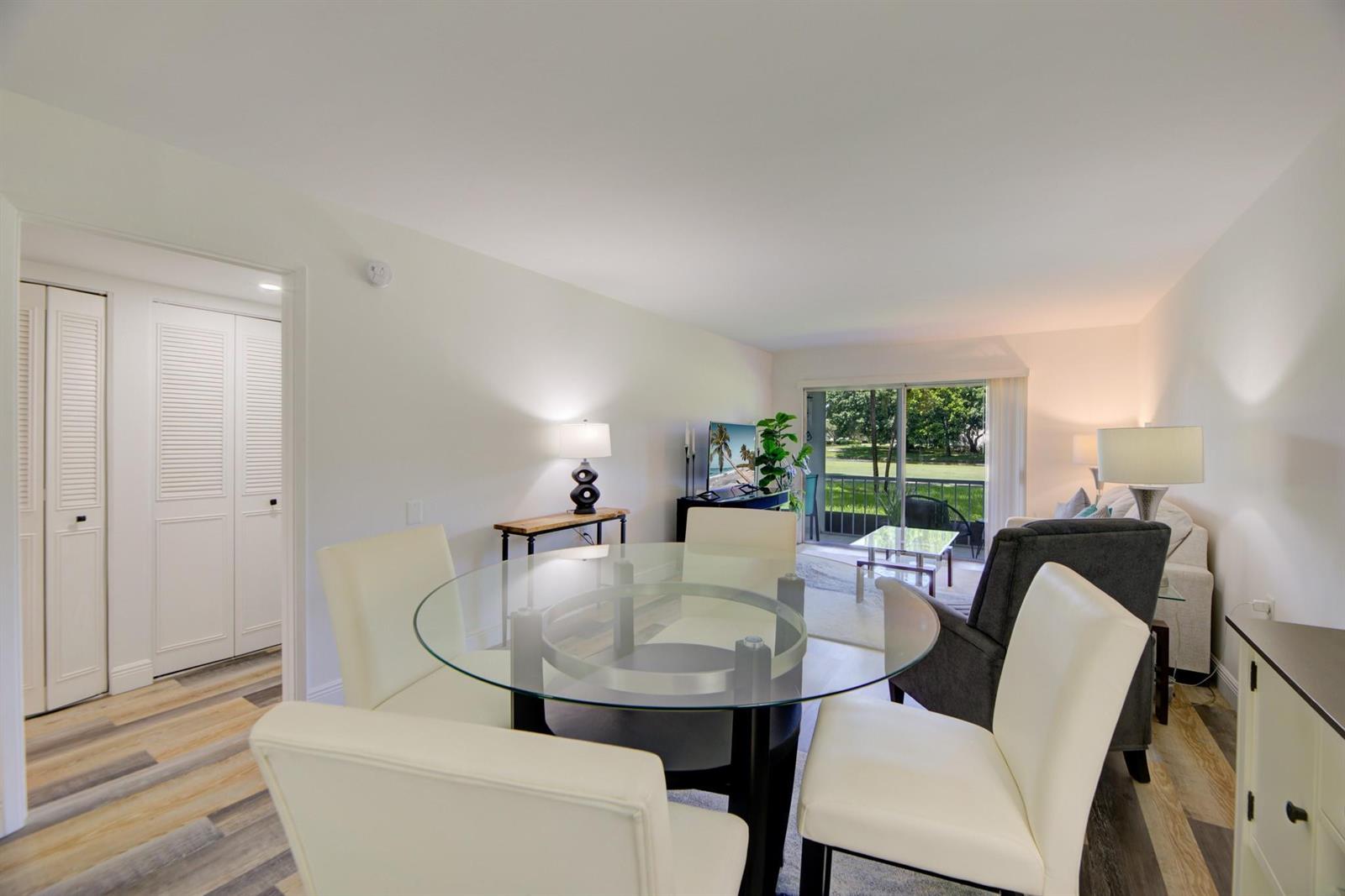 A dining area with a glass table and white chairs opens into a living room — 4502 Martinique Way # E1, Coconut Creek FL 33066, COCONUT CREEK, FL