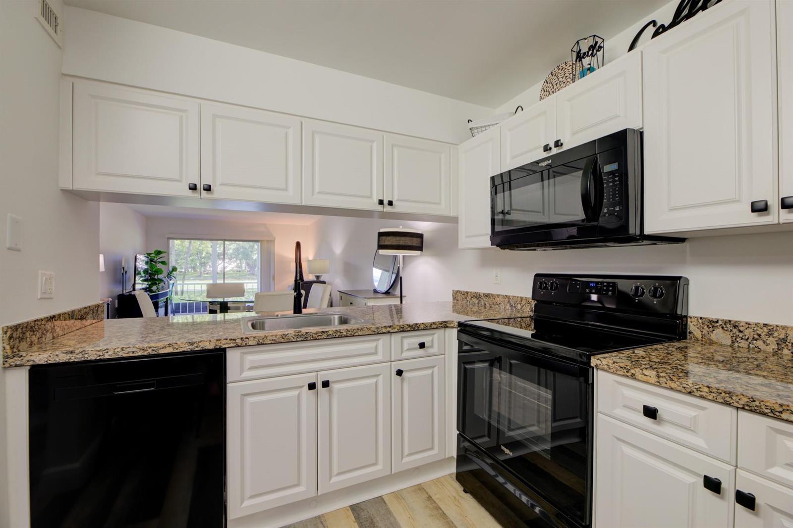 A kitchen with white cabinets, black appliances, and granite countertops overlooks a living area — 4502 Martinique Way # E1, Coconut Creek FL 33066, COCONUT CREEK, FL