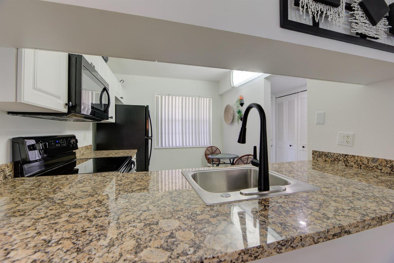 A kitchen features granite countertops, a stainless steel sink, and black appliances — 4502 Martinique Way # E1, Coconut Creek FL 33066, COCONUT CREEK, FL