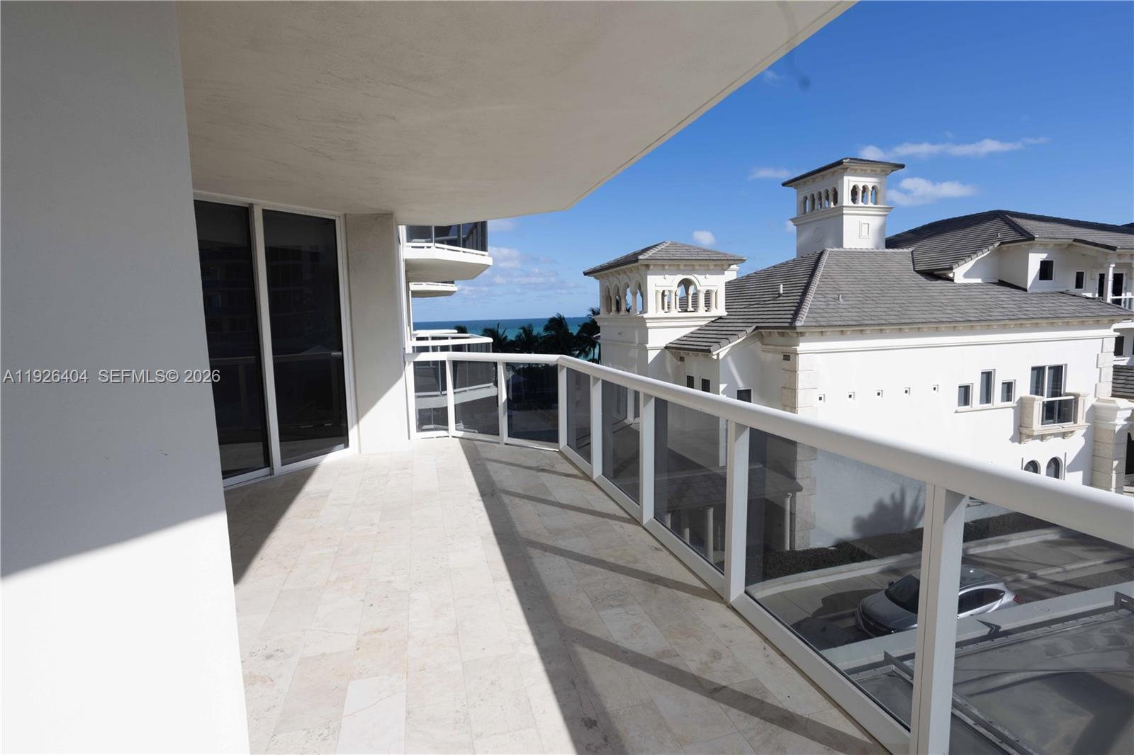 A spacious balcony with stone flooring and a glass railing overlooks a coastal building — 4779 Collins Ave # 504, Miami Beach FL 33140, MIAMI BEACH, FL
