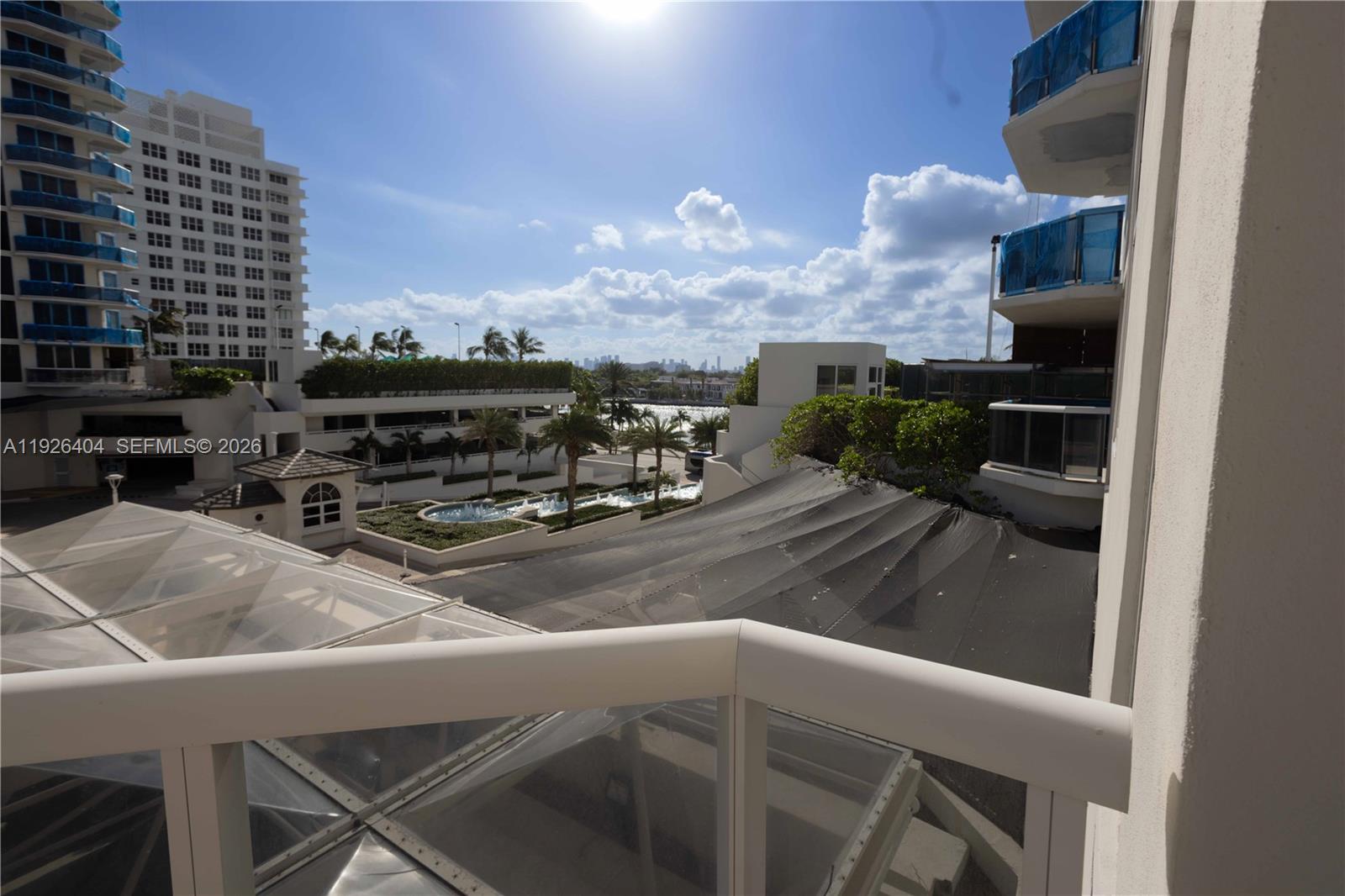 A balcony view overlooks a courtyard with a fountain, palm trees, and nearby buildings — 4779 Collins Ave # 504, Miami Beach FL 33140, MIAMI BEACH, FL
