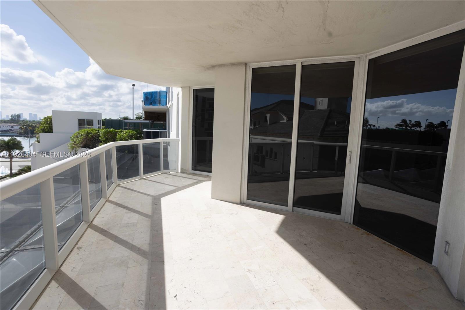 A spacious balcony features light-colored stone flooring, glass railings, and large sliding glass doors — 4779 Collins Ave # 504, Miami Beach FL 33140, MIAMI BEACH, FL