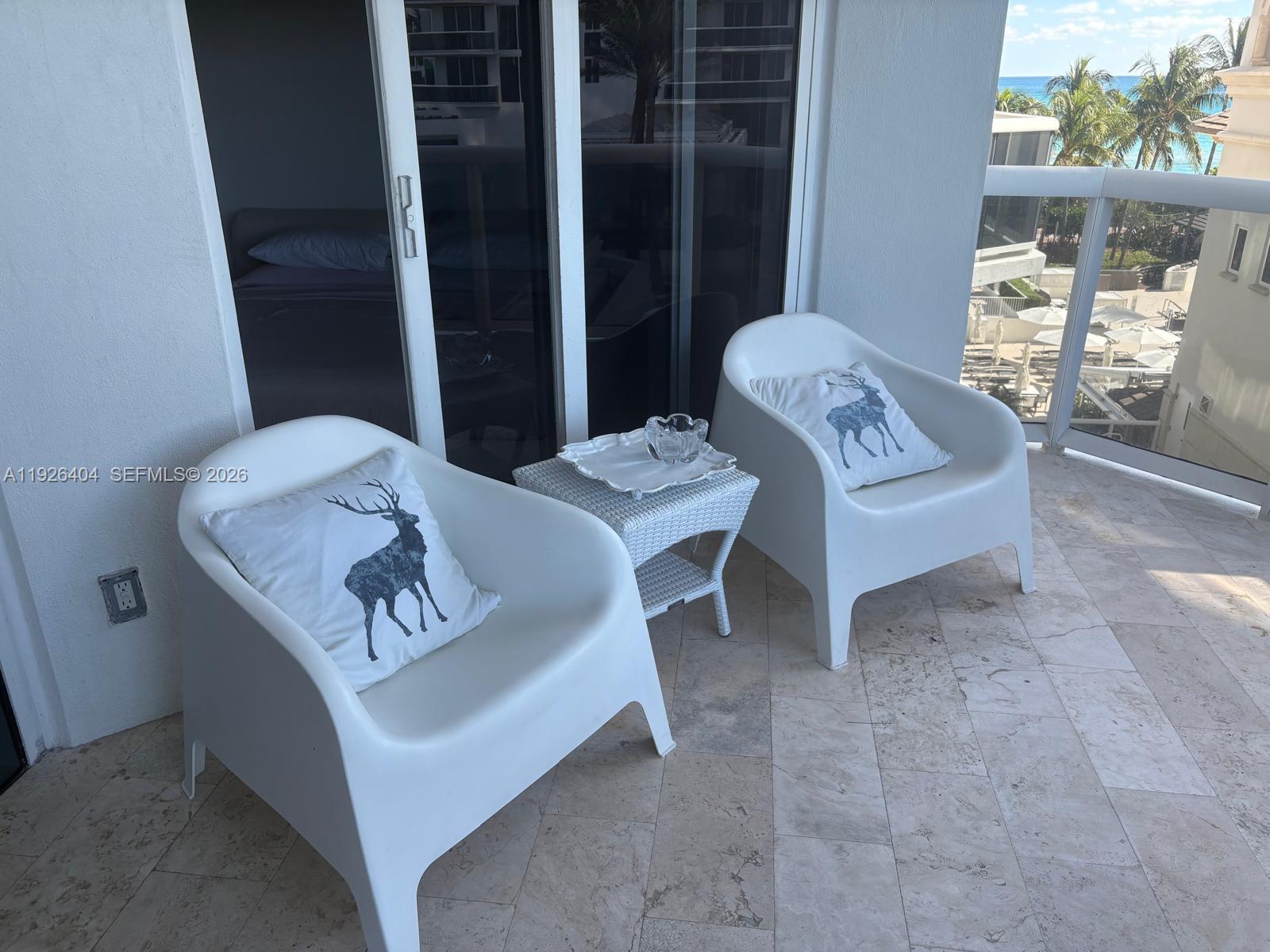 A balcony features two white chairs with deer-print pillows and a small wicker table — 4779 Collins Ave # 504, Miami Beach FL 33140, MIAMI BEACH, FL
