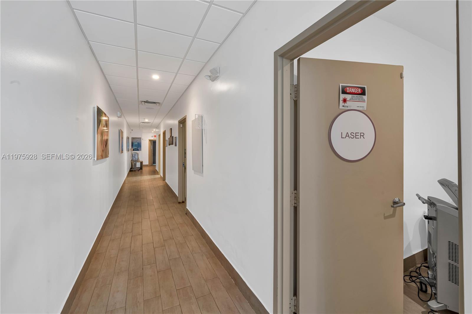 A hallway with wood-look tile flooring leads to several doors, including one marked laser — 3749 NE 163, FL 33160, FL
