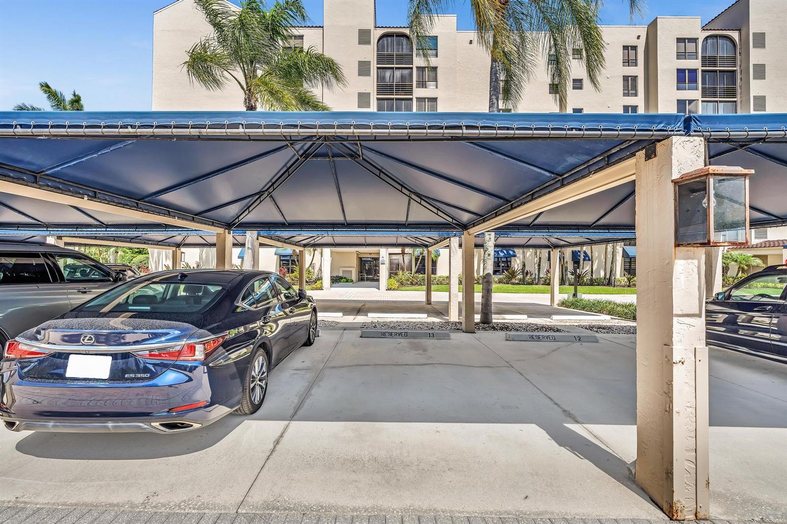 A covered parking area features numbered reserved spaces in front of a multi-story apartment building — 7564 Regency Lake Drive # 202, Boca Raton FL 33433, BOCA RATON, FL