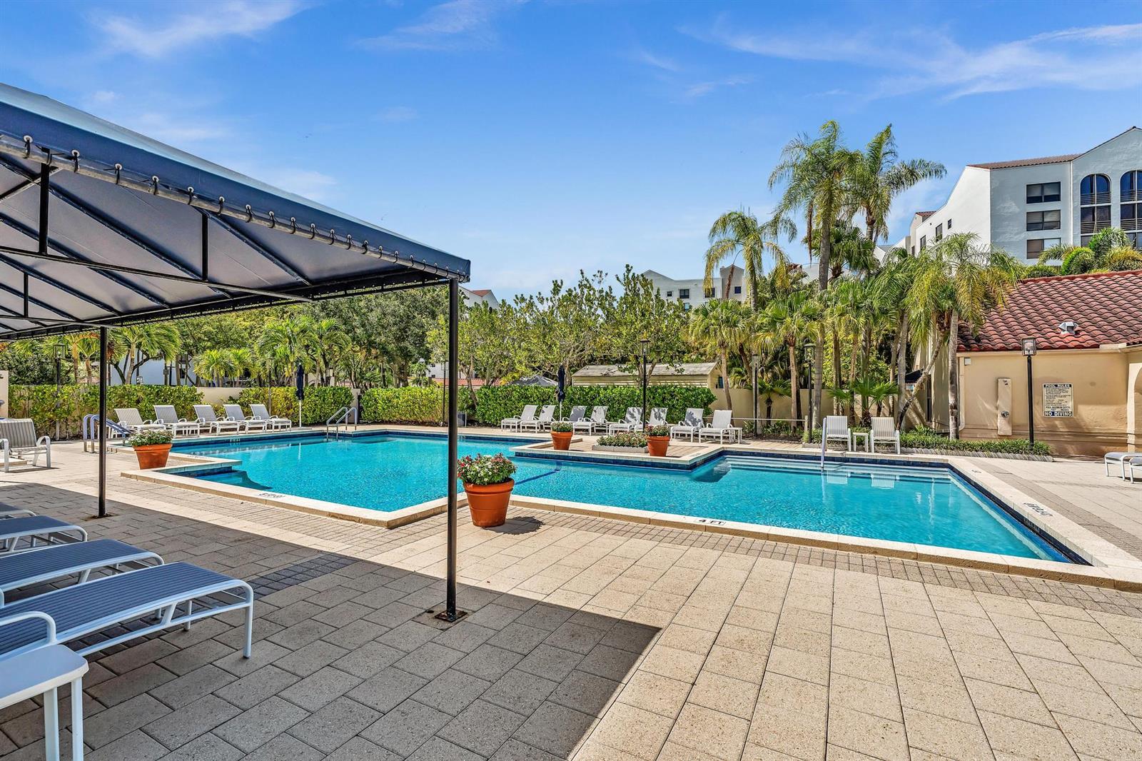An outdoor swimming pool with lounge chairs and a shaded patio area — 7564 Regency Lake Drive # 202, Boca Raton FL 33433, BOCA RATON, FL