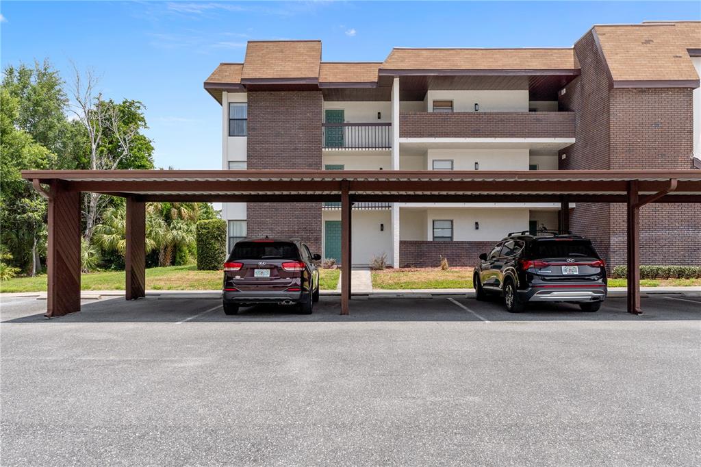 A three-story brick apartment building features a covered parking area with two parked SUVs — 3 CYPRESS RUN UNIT 31C, HOMOSASSA, FL