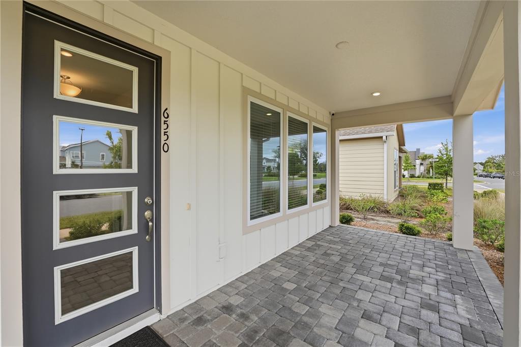 A gray front door with four glass panels sits beside a white-sided wall and porch — 6550 BARNSTORM WAY, ST CLOUD, FL