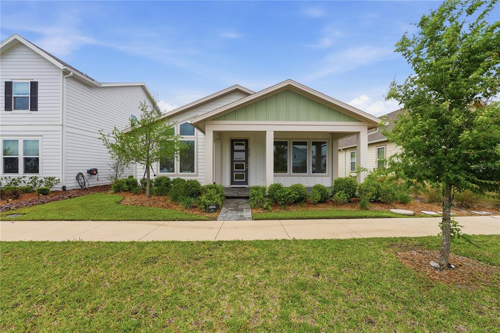 A single-story house with a covered front porch, light siding, and green gable accents — 6550 BARNSTORM WAY, ST CLOUD, FL