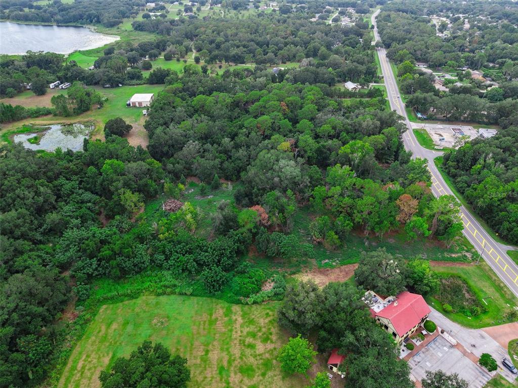 An aerial view shows a wooded lot adjacent to a road and a small lake — COUNTY ROAD 48, YALAHA, FL