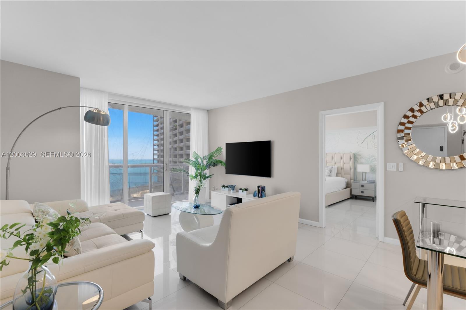 A modern living room features white tile floors, a sectional sofa, and a balcony view — 485 Brickell Ave # 4501, Miami FL 33131, MIAMI, FL
