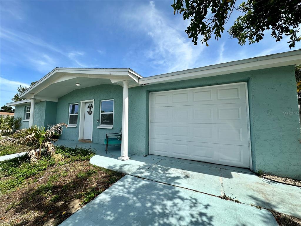 A single-story house with light blue stucco walls, a white garage door, and a front porch — 3240 BRIAR CLIFF DRIVE, HOLIDAY, FL