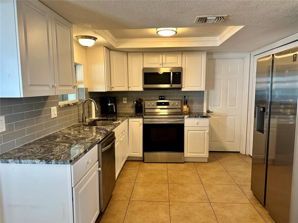 A kitchen features white cabinets, granite countertops, stainless steel appliances, and a gray subway tile backsplash — 3240 BRIAR CLIFF DRIVE, HOLIDAY, FL