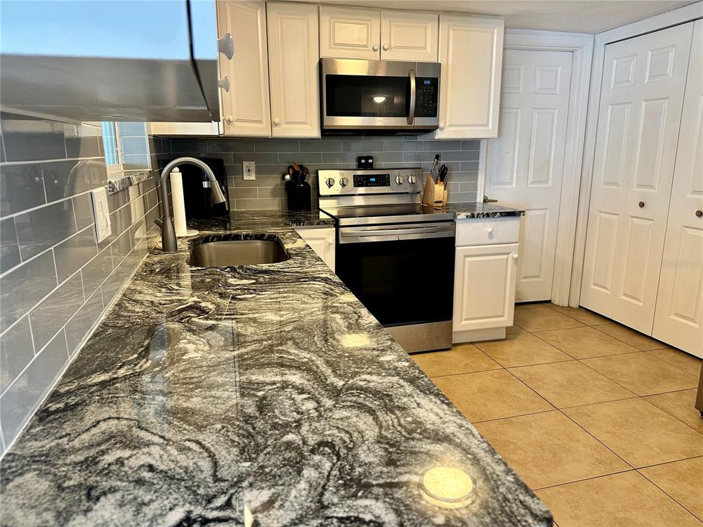 A kitchen features granite countertops, white cabinetry, stainless steel appliances, and a gray tiled backsplash — 3240 BRIAR CLIFF DRIVE, HOLIDAY, FL