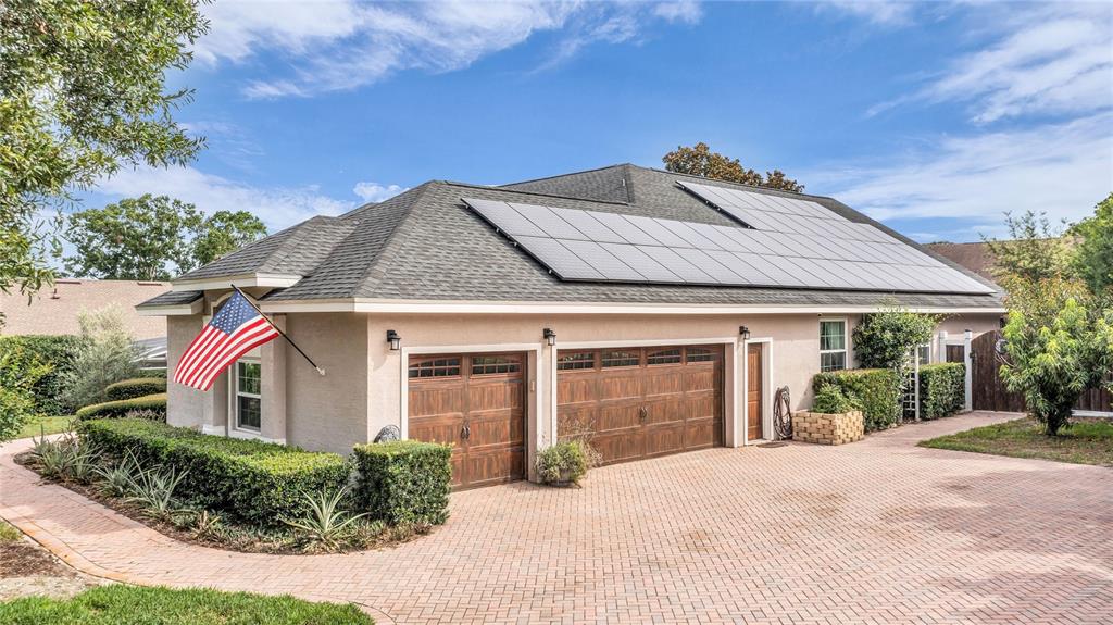 A house exterior features a brick driveway, a three-car garage, and roof-mounted solar panels — 9113 IVEY HILL COURT, ORLANDO, FL