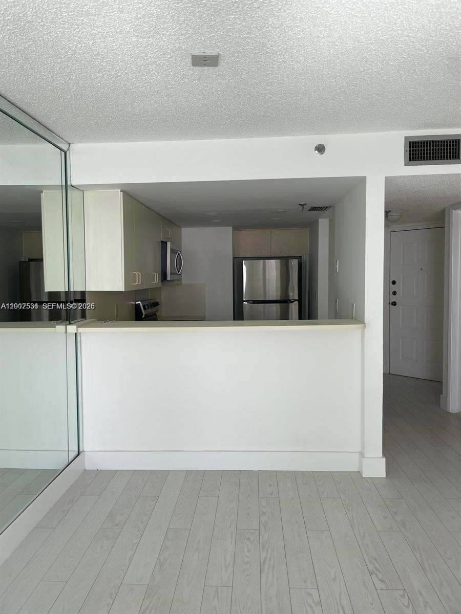 A kitchen with stainless steel appliances and a breakfast bar overlooks a living area — 5880 Collins Ave # 1006, Miami Beach FL 33140, MIAMI BEACH, FL