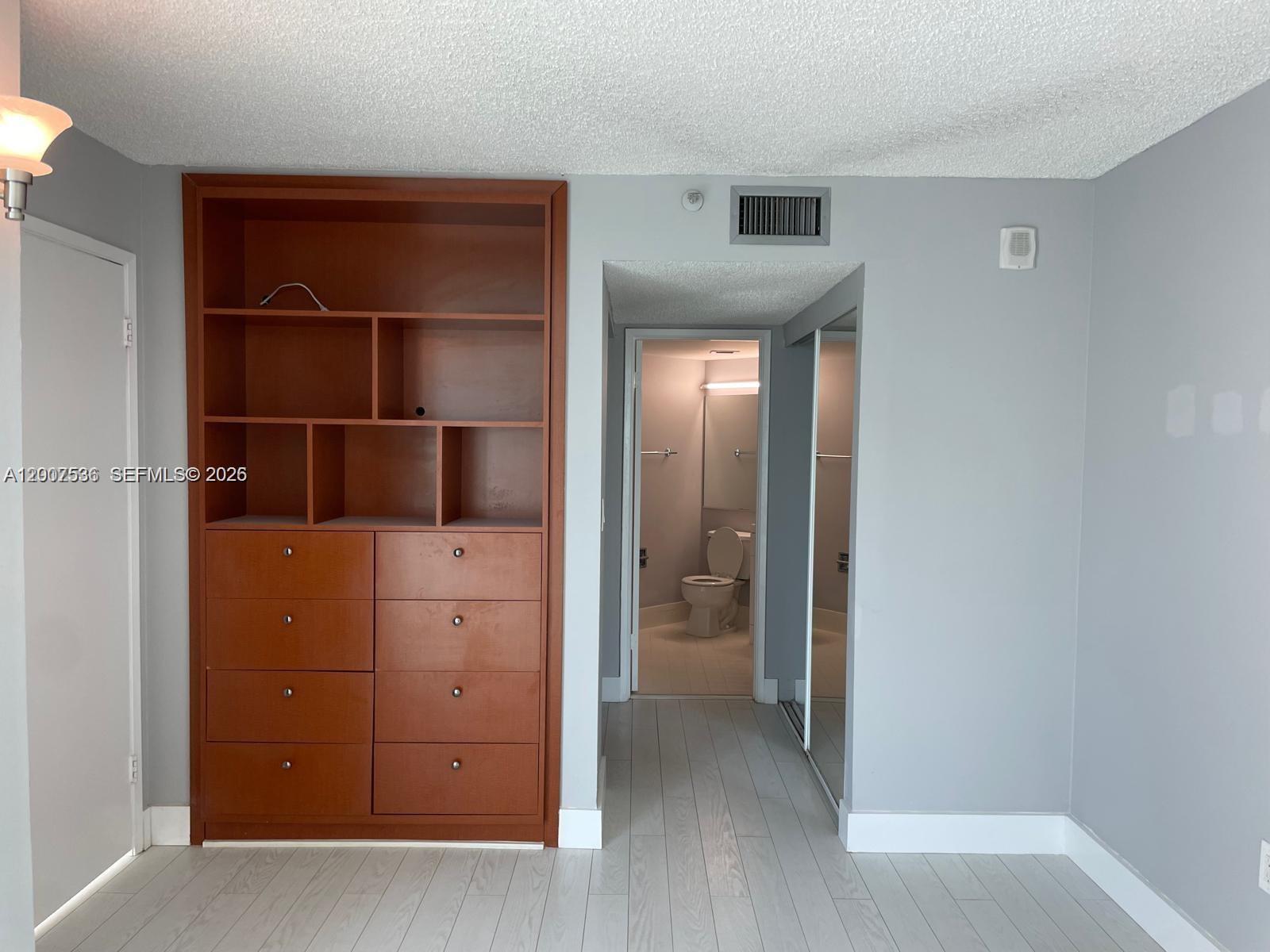 A room features a built-in wooden shelving unit, light gray flooring, and a doorway leading to a bathroom — 5880 Collins Ave # 1006, Miami Beach FL 33140, MIAMI BEACH, FL