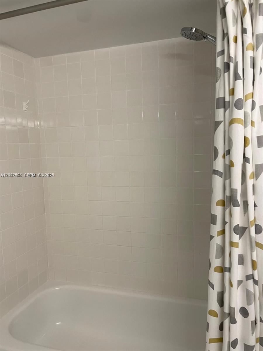 A white tiled bathtub and shower enclosure with a patterned curtain — 5880 Collins Ave # 1006, Miami Beach FL 33140, MIAMI BEACH, FL