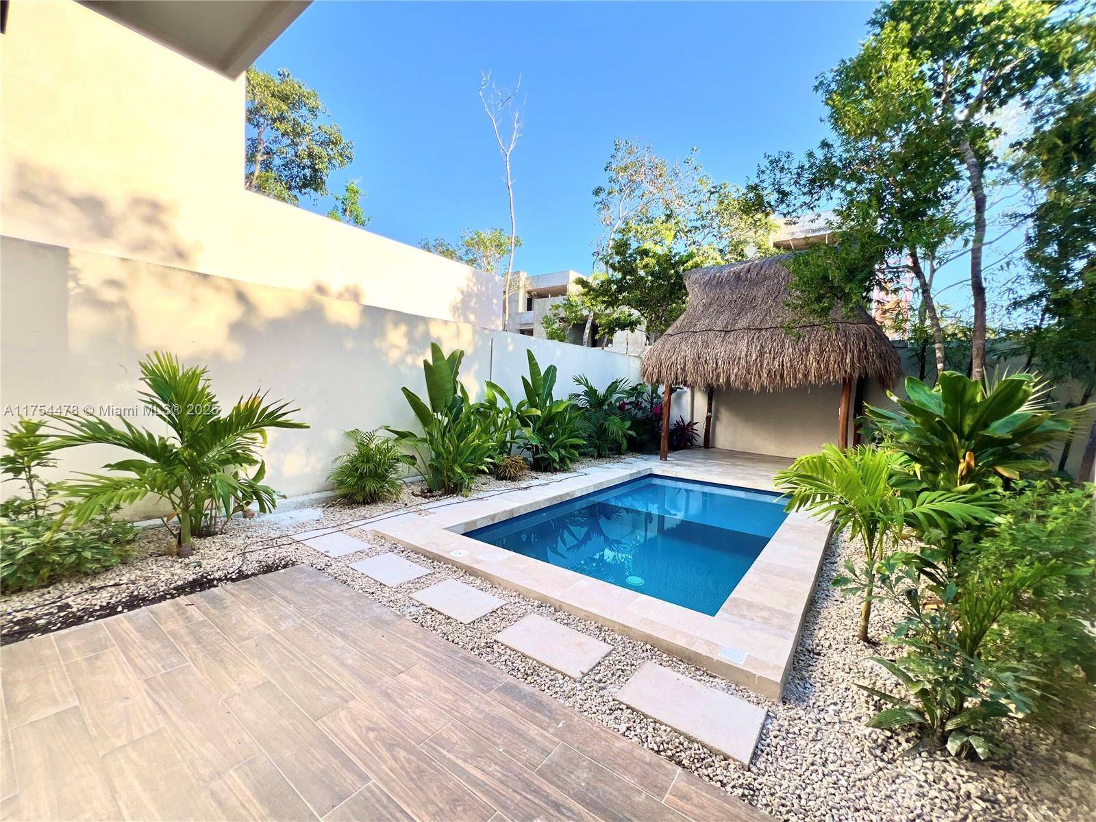 A small rectangular swimming pool sits in a landscaped backyard with a thatched-roof palapa — Kaybe Tulum Kaybe Tulum, TX 77760, TX