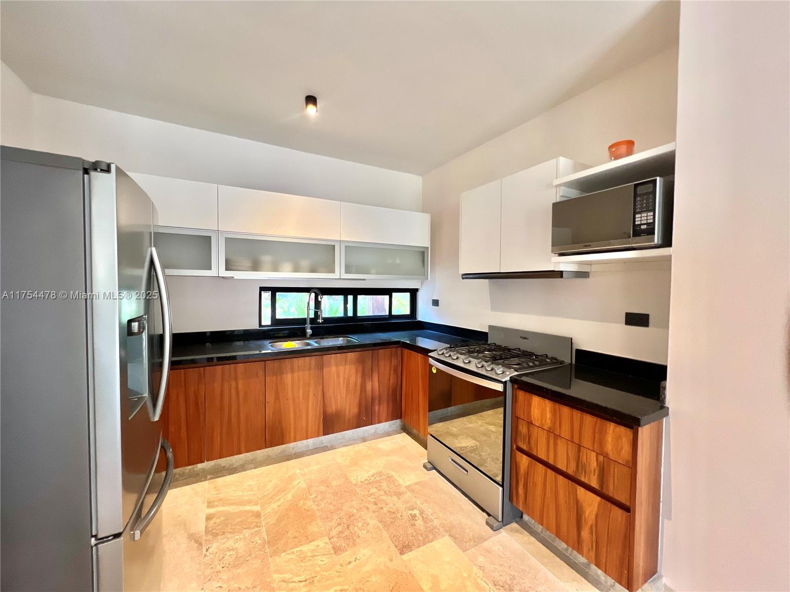 A kitchen features wood cabinets, black countertops, stainless steel appliances, and light-colored stone flooring — Kaybe Tulum Kaybe Tulum, TX 77760, TX
