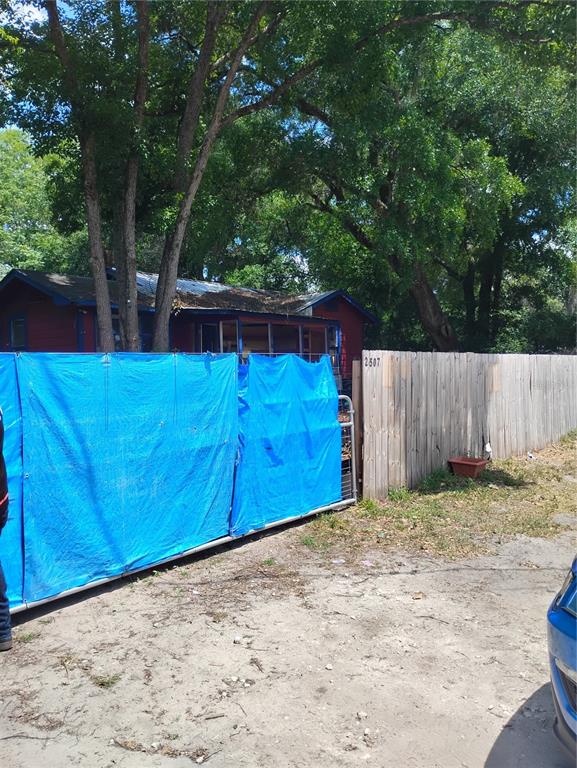 A red house is partially obscured by a blue tarp fence and large trees — 2507 N MAGNOLIA AVENUE, OCALA, FL