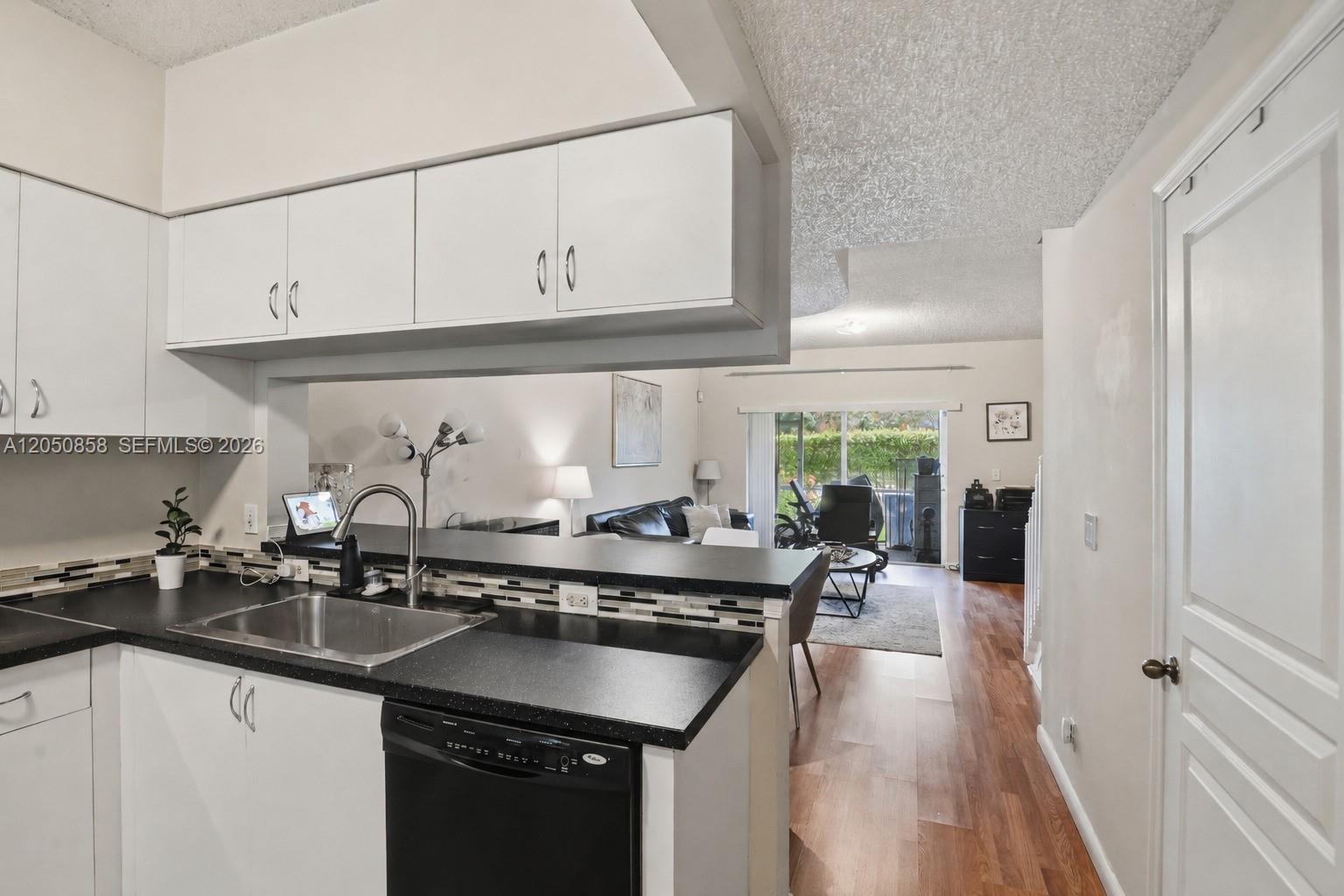 A kitchen with black countertops and white cabinets overlooks a living area with wood flooring — 21 Simonton Cir, Weston FL 33326, WESTON, FL
