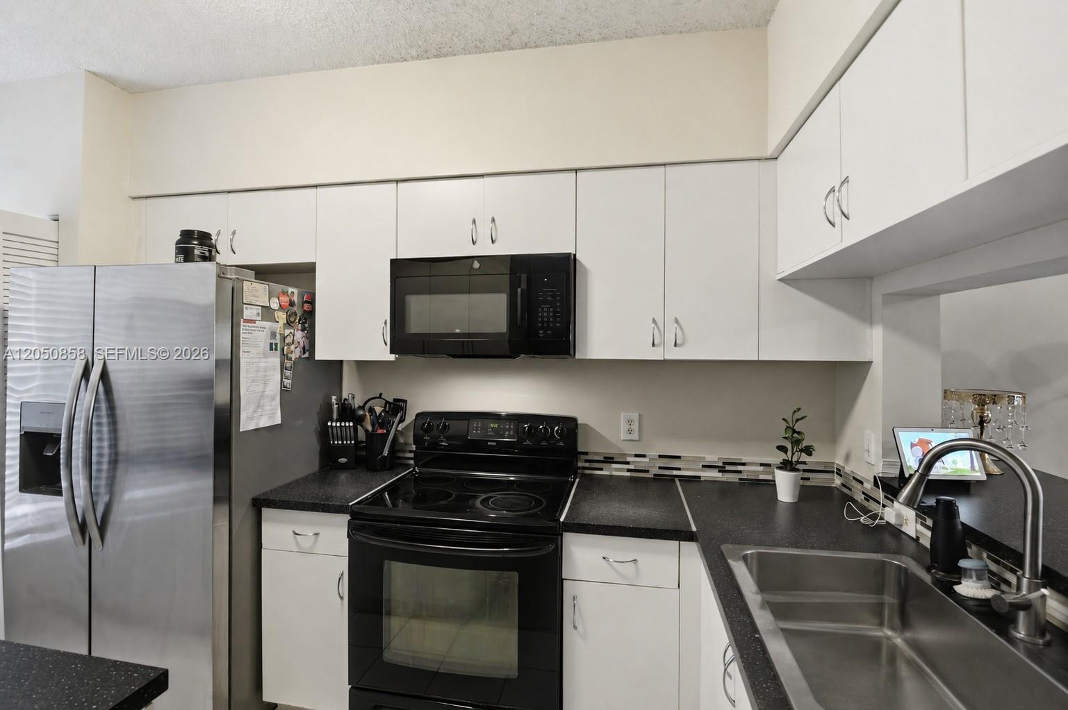 A kitchen features white cabinets, black appliances, dark countertops, and a stainless steel sink — 21 Simonton Cir, Weston FL 33326, WESTON, FL