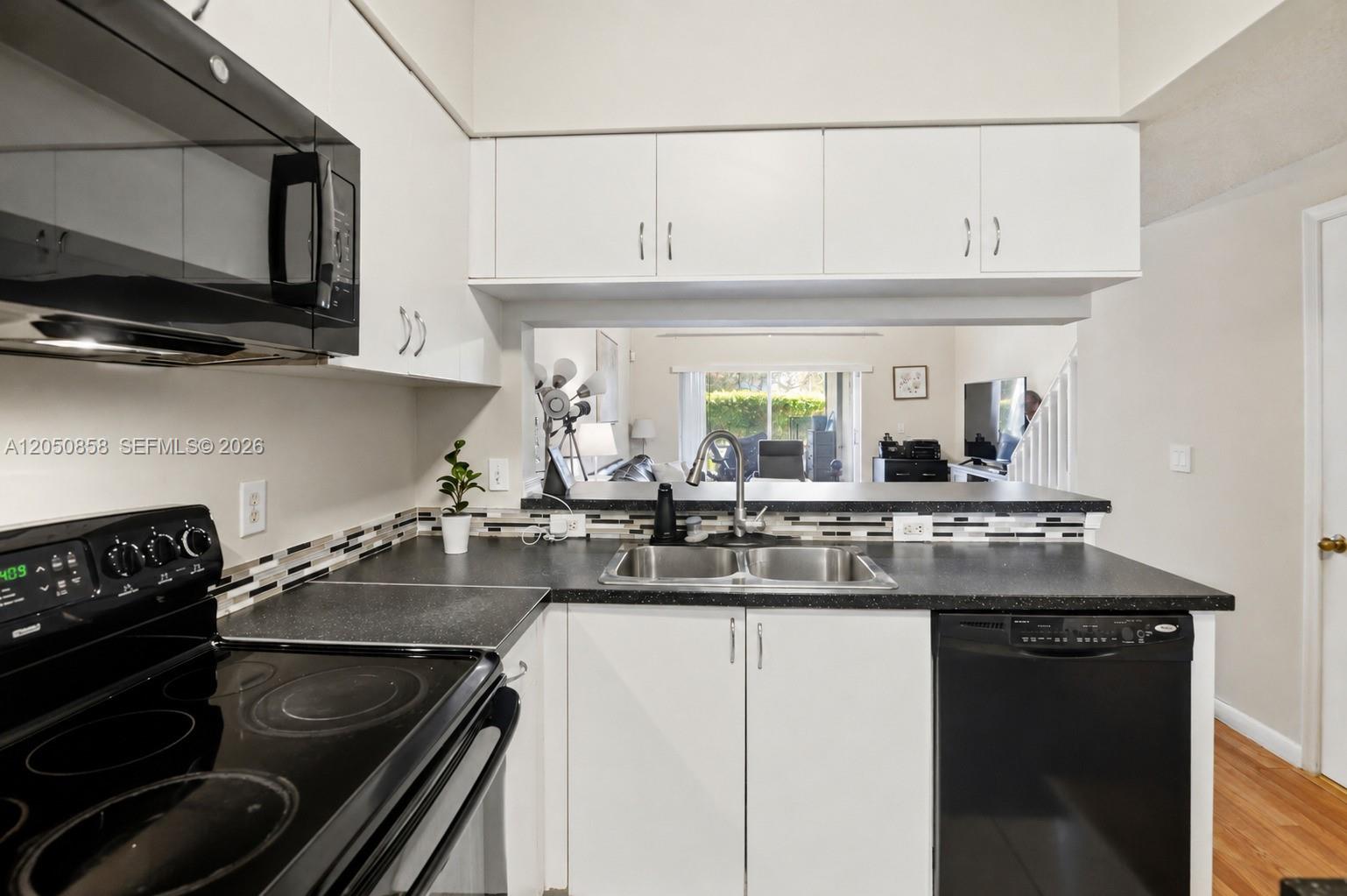 A kitchen features white cabinets, black appliances, a dark countertop, and a pass-through window — 21 Simonton Cir, Weston FL 33326, WESTON, FL
