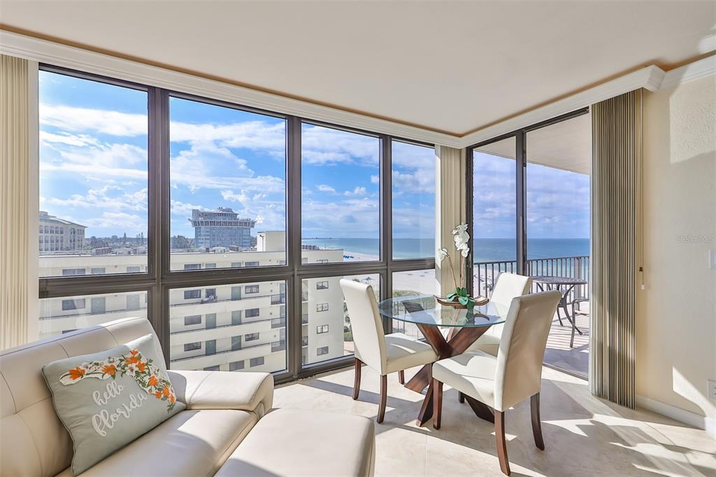 A sunlit dining area with floor-to-ceiling windows overlooking the ocean and a nearby building — 5396 GULF BOULEVARD UNIT 701, ST PETE BEACH, FL