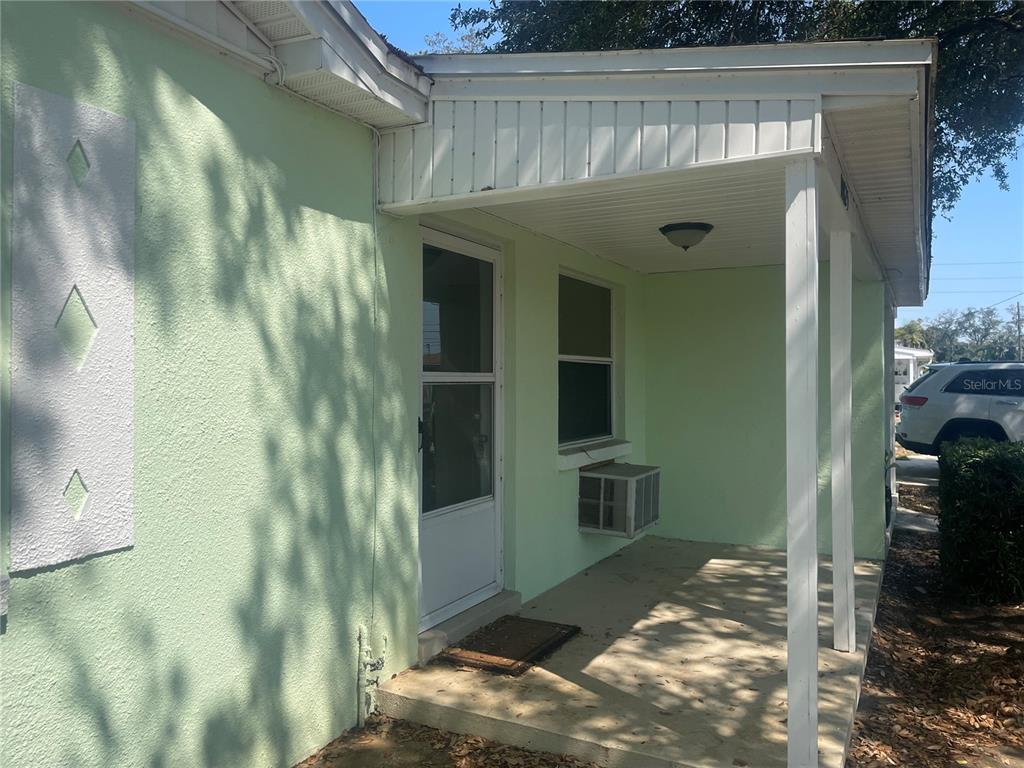 A light green house features a covered front porch with a white door and window — 10825 NAVAJO DRIVE, ST PETERSBURG, FL
