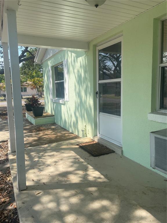 A covered concrete porch leads to a white storm door on a light green house — 10825 NAVAJO DRIVE, ST PETERSBURG, FL