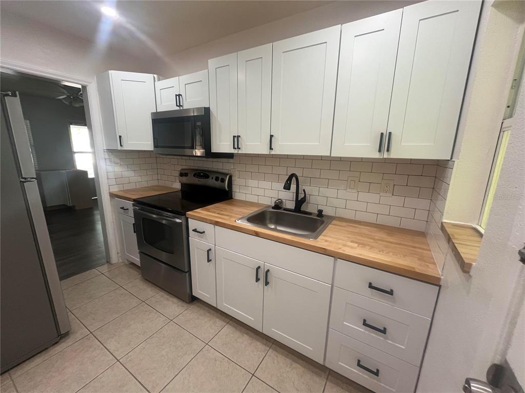A kitchen features white shaker cabinets, butcher block countertops, stainless steel appliances, and subway tile — 10825 NAVAJO DRIVE, ST PETERSBURG, FL