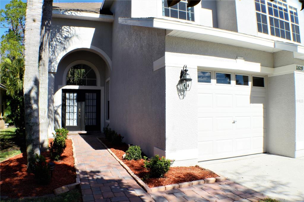 A two-story house exterior features a paved walkway, arched entryway, and a single-car garage — 11609 GREENSLEEVE AVENUE, TAMPA, FL