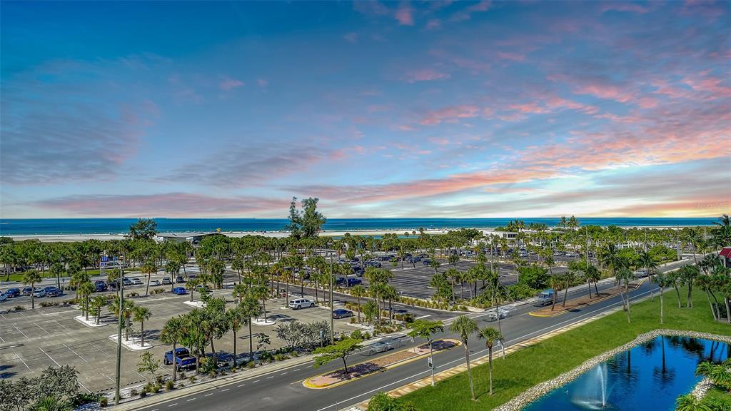 An elevated view of a parking lot, palm trees, a pond, and the ocean beyond — 1055 BEACH ROAD UNIT B602, SARASOTA, FL