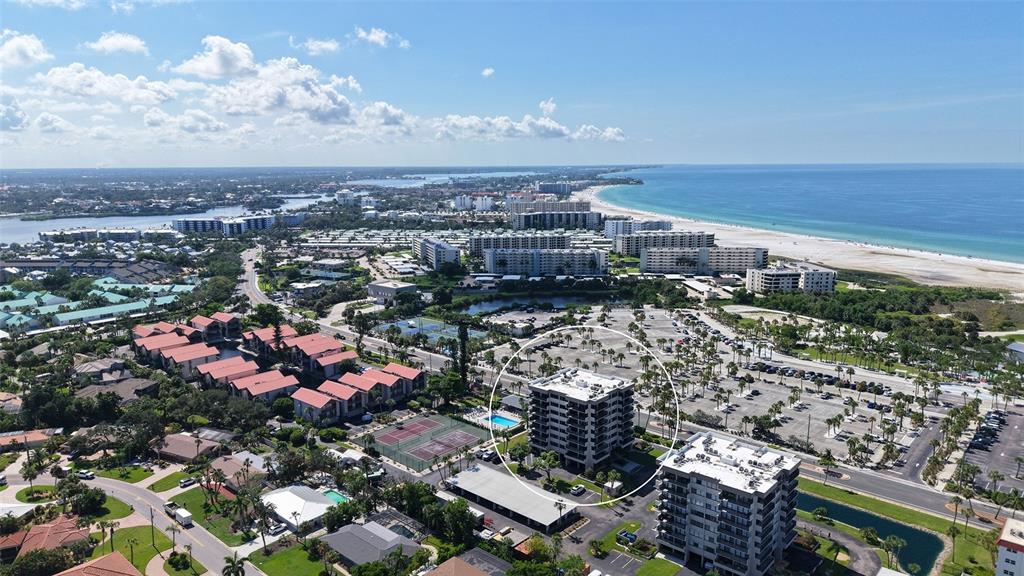 An aerial view shows a multi-story residential building circled in a coastal neighborhood — 1055 BEACH ROAD UNIT B602, SARASOTA, FL