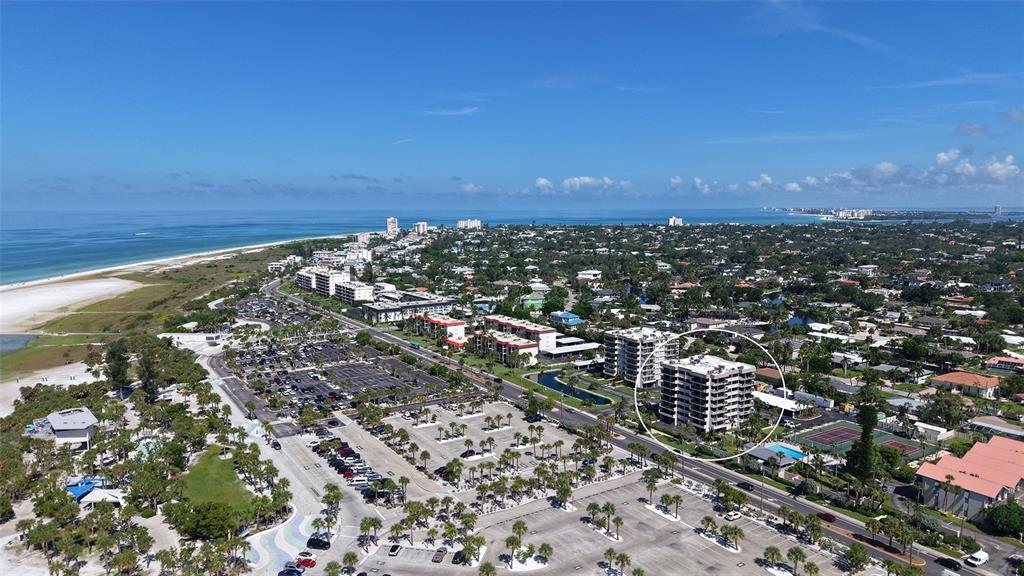 An aerial view shows a multi-story residential building circled near a beach and parking lot — 1055 BEACH ROAD UNIT B602, SARASOTA, FL