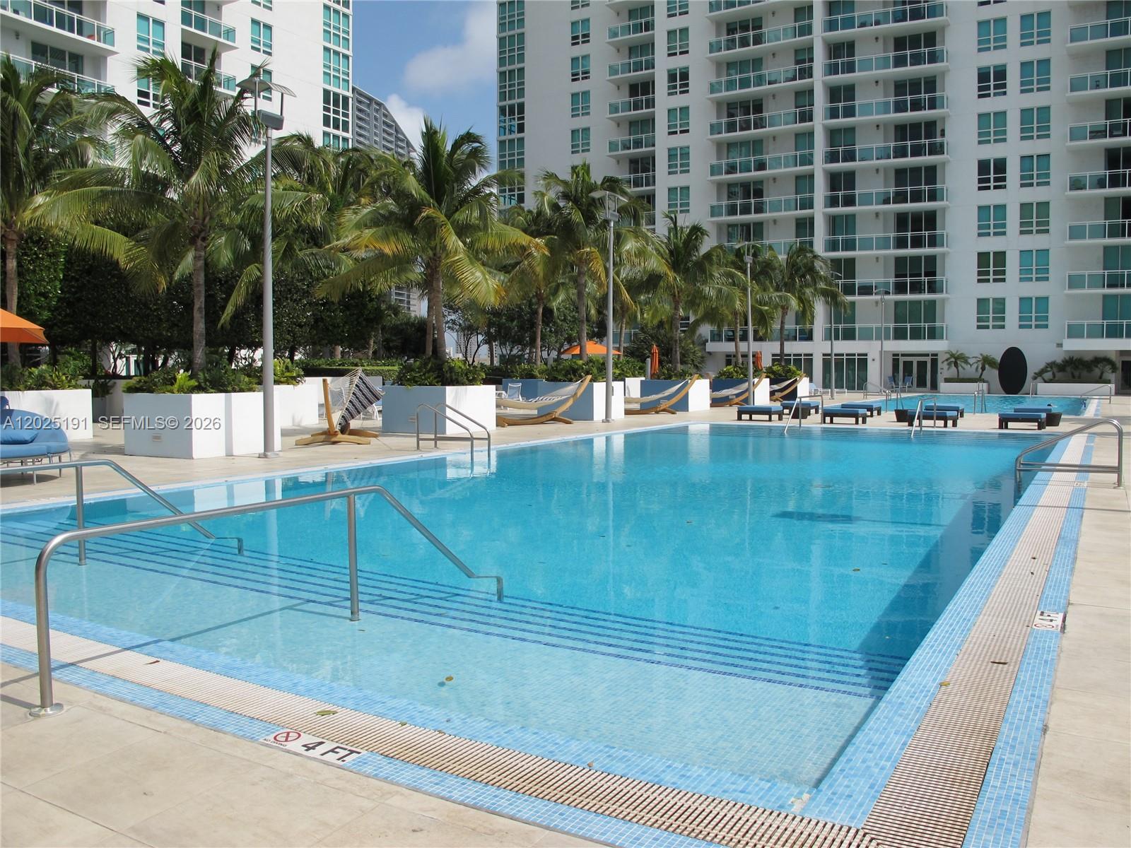 A rectangular swimming pool with steps and metal railings is surrounded by palm trees and buildings — 951 Brickell Ave # 1209, Miami FL 33131, MIAMI, FL