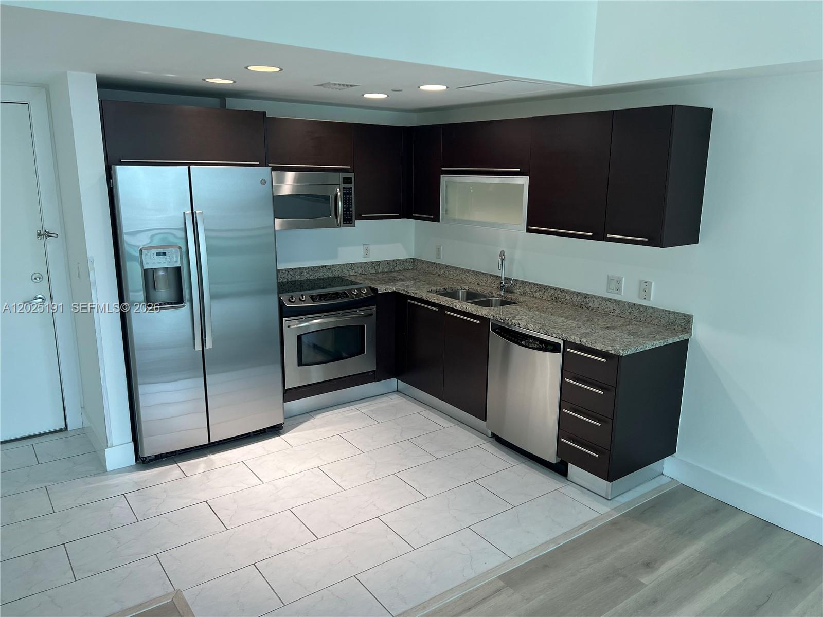 A kitchen features dark wood cabinets, stainless steel appliances, and granite countertops over tiled floors — 951 Brickell Ave # 1209, Miami FL 33131, MIAMI, FL