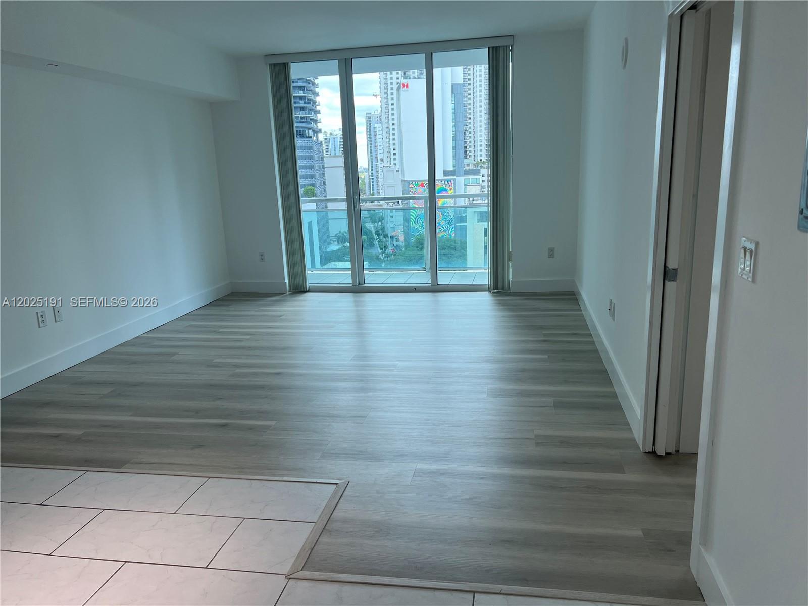 An empty living area features light wood-look flooring, white walls, and a balcony with city views — 951 Brickell Ave # 1209, Miami FL 33131, MIAMI, FL