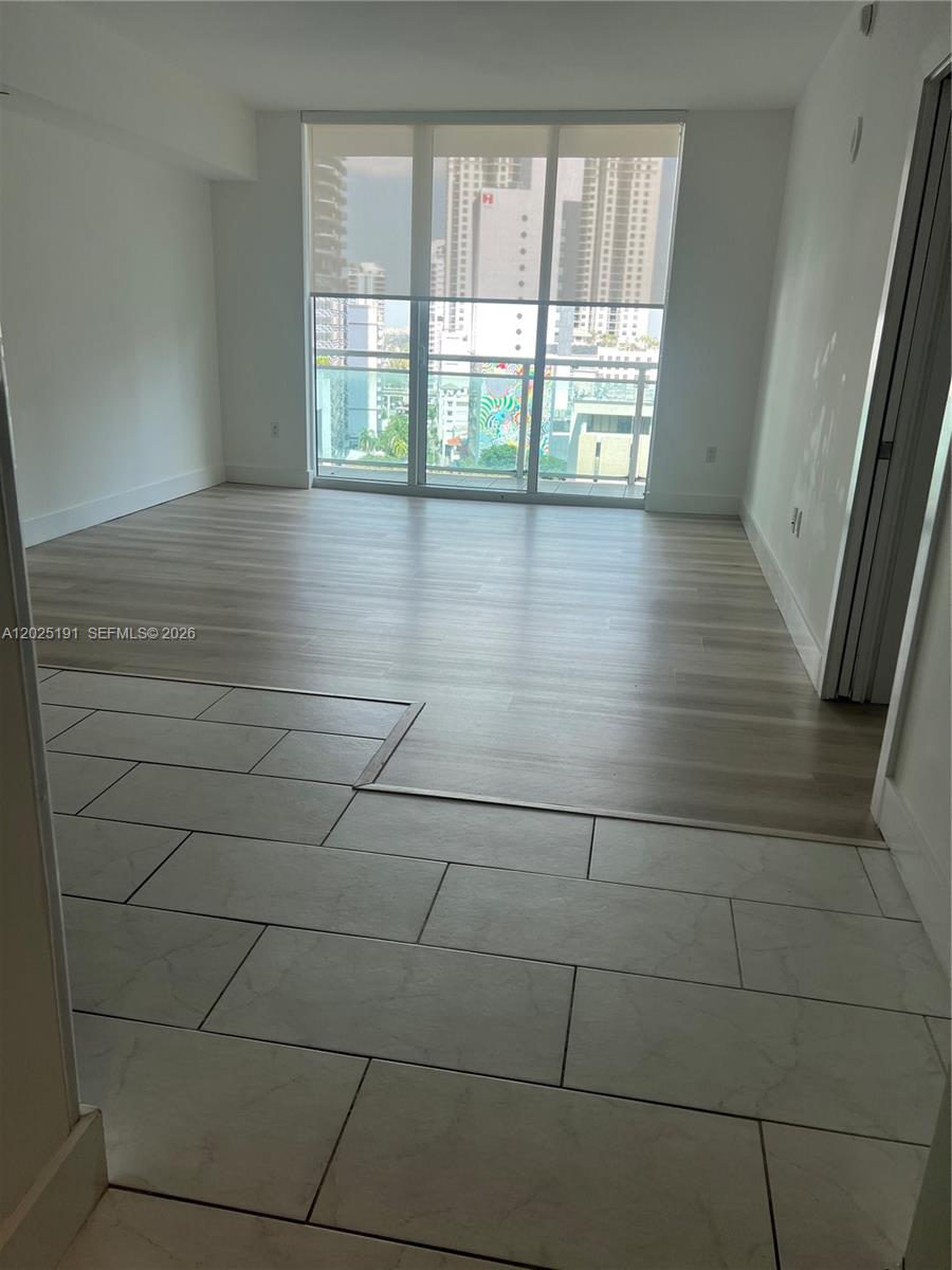 An empty room features light wood-look flooring, white walls, and floor-to-ceiling windows with city views — 951 Brickell Ave # 1209, Miami FL 33131, MIAMI, FL